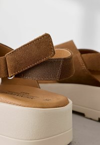 I sandali platform in suede marrone presentano una cinghia regolabile con una superficie testurizzata, una soletta beige liscia e una robusta suola bianca.
