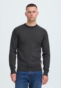 Dunkelgrauer Pullover, gestrickte Textur, runder Ausschnitt, lange Ärmel, figurbetontes Design, mit einem kleinen braunen Logo-Patch am Saum.