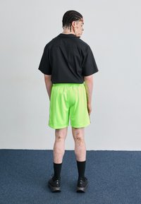 Black short-sleeve shirt, neon green shorts, black crew socks, and athletic shoes. Casual sportswear displayed from the back.
