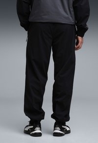 Zwart, loszittende broek met een elastische tailleband, zakken met rits, gemaakt van lichtgewicht stof. Gecombineerd met zwart-witte sneakers.