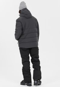 Graue isolierte Jacke mit Kapuze, kombiniert mit schwarzen wasserdichten Hosen. Verfügt über ein eng anliegendes Design und strukturierten Stoff. Schwarze Schuhe vervollständigen den Look.