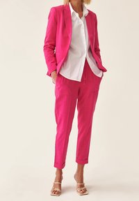 Jasně růžový přizpůsobený oblek s klopami, v kombinaci s bílou košilí s knoflíky. Obsahuje volně střižené kalhoty a metalické sandály na řemínky.