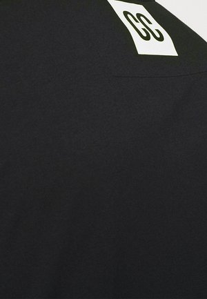 Czarna tkanina z białą prostokątną etykietą, na której znajduje się liczba 23 w pogrubionym czarnym tekście.