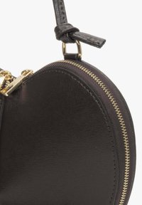 Czarna okrągła torebka wykonana z teksturowanej skóry, z złotym zamkiem błyskawicznym i węzłowym paskiem. Kompaktowy design o gładkim wykończeniu.