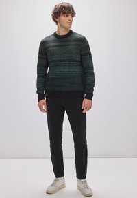 Mörkgrön stickad tröja med horisontell randig mönster, rund hals, och ribbade ärmslut, tillsammans med svarta byxor och vita sneakers.