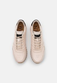 Světlé béžové tenisky s texturovaným svrškem s embosovaným krokodýlím vzorem, černými detaily a korkovou stélkou, s tónovými tkaničkami a gumovou podrážkou.