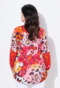 Chemise colorée à manches longues avec un mélange de motifs d'imprimé animal rouge, rose et orange. Ourlet arrondi et coupe décontractée avec un détail textuel au dos.