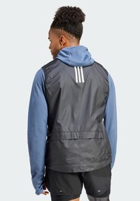 Svart lett vest over en blå langermet skjorte, med tre hvite striper på baksiden og et ventilert design. Svarte shorts synlige under.