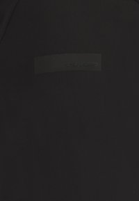 Maglietta sportiva nera realizzata in un tessuto liscio e texture, con un evidente logo rettangolare nero opaco sul davanti.