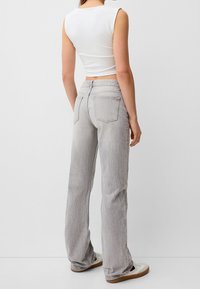 Jeans grigi chiari a campana con una finitura testurizzata, cinque tasche e vita media, abbinati a un top aderente bianco senza maniche.