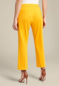 Gele, op maat gemaakte broeken met een rechte pijpdesign, met een gladde textuur en een middelhoge tailleband, gecombineerd met bruine hoge hakken.