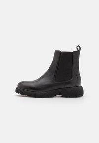 Botas de tobillo de cuero negro con paneles laterales elásticos y una lengüeta. Presentan una suela gruesa y texturizada para mayor agarre y comodidad.