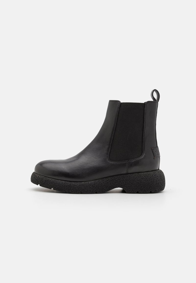 Botas de tobillo de cuero negro con paneles laterales elásticos y una lengüeta. Presentan una suela gruesa y texturizada para mayor agarre y comodidad.
