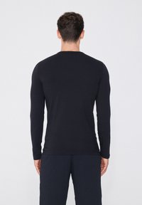 Schwarzes Langarmshirt aus weichem Stoff, mit Rundhalsausschnitt und schlanker Passform, kombiniert mit dunklen Hosen. Minimalistischer Stil.