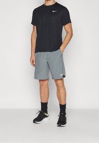 Schwarzes Nike T-Shirt, kurzärmlig, und graue Shorts mit Taschen. Schwarze und gelbe Sneakers. Einfaches Design, keine sichtbaren Muster oder Logos.