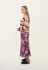 Gestreifter Strickpullover in Beige und Burgunder, kombiniert mit einem floralen lila Rock, grauen Socken und dunkelbraunen Holzclogs, seitlich dargestellt.