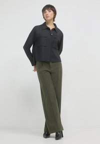 Schwarzes cropped Shirt mit zwei Brusttaschen, kombiniert mit olivgrünen, weit geschnittenen Cordhosen. Glatte Texturen, elegantes Design und subtiler Glanz.