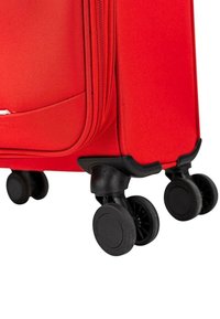 Maleta roja con ruedas, exterior de tela texturizada, equipada con ruedas giratorias negras de movimiento suave y esquinas reforzadas para mayor durabilidad.