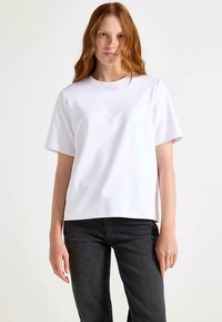 White short-sleeve t-shirt with a round neckline and loose fit, made of smooth cotton fabric, displayed with dark jeans.