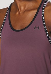 Lila idrottstopp i polyester med en slät yta, med svarta band prydda med vit "Under Armour"-logotyp.