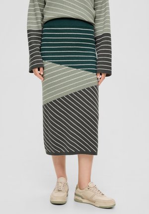 Strickrock mit diagonalen grünen, grauen und weißen Streifen; gerippter Bund; kombiniert mit beigen Sneakers. Glatte Textur und figurbetonter Schnitt.
