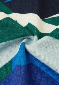 Tkanina dzianinowa posiada wzór niebieskich, zielonych i kremowych kształtów, prezentując miękką teksturę z lekko podwiniętym brzegiem.