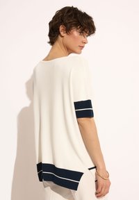 Luźna, biała bluzka dzianinowa z granatowymi paskami przy mankietach i u dołu. Posiada zaokrąglony dekolt i boczne rozcięcia dla większej swobody ruchów.