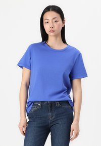 T-shirt à col rond à manches courtes en coton bleu uni, présentant une coupe décontractée et des détails de couture minimes, associé à un jean en denim noir.