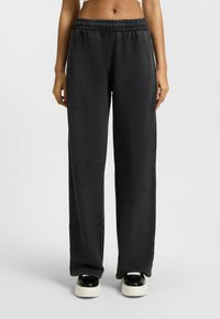 Pantalons de survêtement noirs, amples et confortables avec une taille élastique, fabriqués en matériau doux. Dotés de poches latérales et d'un design à jambe droite.