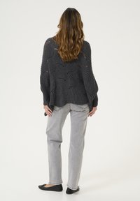 Suéter gris de punto con un patrón circular texturizado, combinado con jeans rectos gris claro y bailes negros. El suéter tiene mangas anchas.