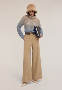 Sweter dziergany z gradientem w odcieniach niebieskiego i beżu, z golfem, zestawiony z szerokimi beżowymi spodniami sztruksowymi. Dodatki to brązowy pasek i beżowa kapelusz typu bucket.