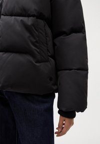 Black puffer jacket featuring a quilted design, zippered front, side pockets, and ribbed cuffs. Material appears smooth and insulated.