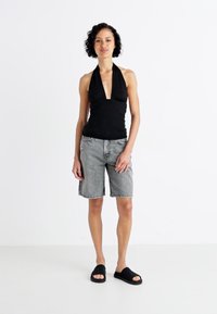 Svart halterneck-topp, grå denimshorts, svarte sandaler. Enkelt design, myk stoff og avslappet passform. Nøytrale farger, ingen synlige mønstre.