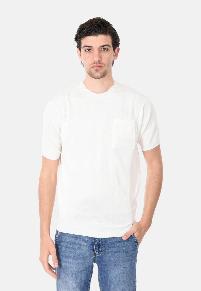 Maglione bianco lavorato a maglia a maniche corte con scollo rotondo e taschino sul petto, abbinato a jeans in denim blu.