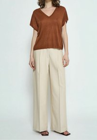 Camiseta marrón de escote en V con mangas cortas, combinada con pantalones de pierna ancha beige. Textura suave, corte holgado y diseño minimalista.