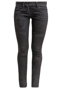 Schwarze Jeans aus Denim mit einem figurnahen Design, ausgestattet mit zwei großen Knieflicken und traditioneller Taschenanordnung. Der Stoff hat einen leichten Glanz und eine Textur.