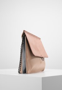 Světle růžová kožená kabelka s klopovým uzavíráním, šedým interiérem, řetízkovým popruhem a minimalistickým designem. Hladký povrch bez viditelných vzorů.