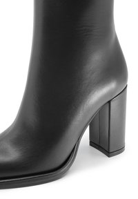 Stivaletto in pelle nera con punta arrotondata e tacco quadrato. Texture liscia con una leggera lucentezza, dettagli di cucitura minimi.