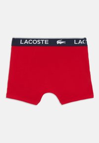 Piros férfi boxer alsó, tengerészkék derékkal, rajta a "LACOSTE" felirattal és logóval. Puha pamut anyag, sima textúrával.