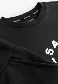 Sudadera negra con texto parcial en blanco, cuello redondo acanalado y puño de manga acanalado, colocada plana sobre una superficie blanca.