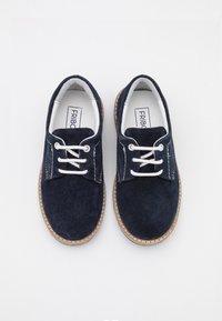 Coppia di scarpe in pelle scamosciata blu navy con lacci bianchi e suole cucite color cuoio, viste dall'alto su sfondo bianco.