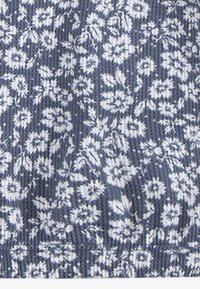 Tela azul con un patrón floral blanco, que presenta un relieve texturizado y un dobladillo elástico recogido. El diseño enfatiza motivos naturales en toda la pieza.