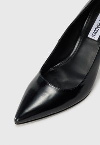 Black glossy pointed-toe high heel shoe with smooth leather finish and visible inner sole label on a white background.