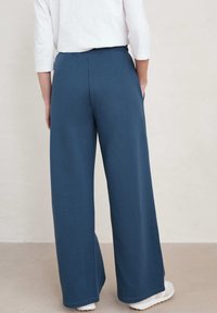 Breda byxor i mörkblått tyg, med elastisk midja och en slät, mjuk textur. Enfaldig design utan ytterligare mönster.