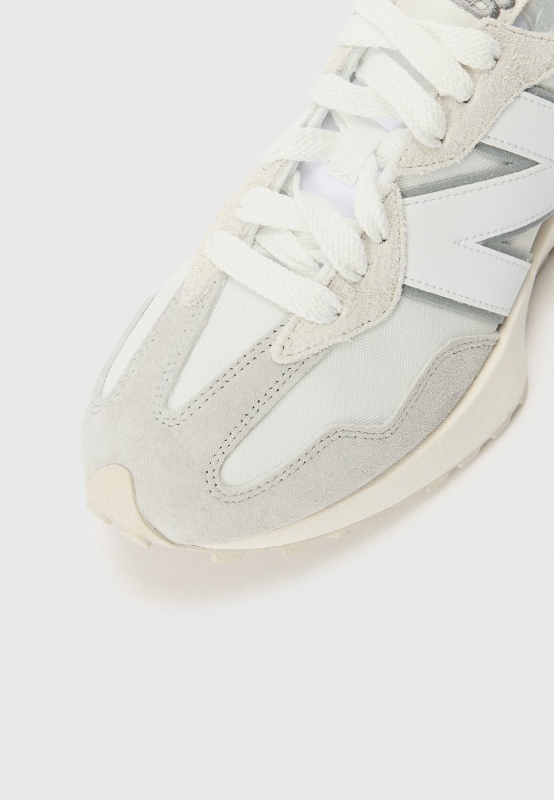 Chaussure de sport grise en matériaux en mesh et en suède, avec une semelle blanche, des lacets bien visibles et un logo sur le côté dans un design épuré.