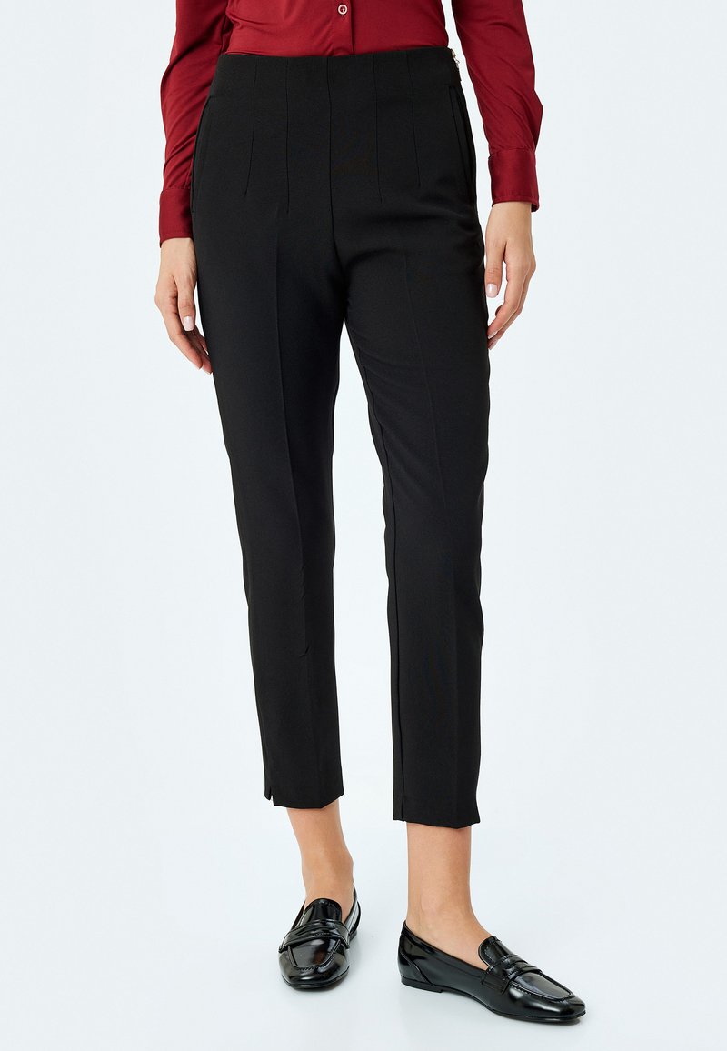 Pantalons noirs ajustés avec des détails plissés, coupe slim et longueur raccourcie. Associés à des mocassins noirs, portés avec une chemise boutonnée bordeaux.