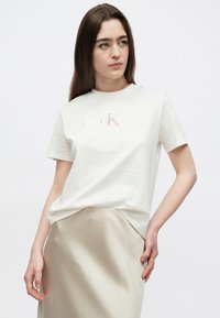 Balta kokvilnas īsroku T-krekls ar mazu rozā cK logotipu krūšu daļā. Kombinēts ar gludu bēšu svārku.