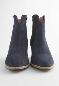 Încălțări ankle din suede bleumarin, cu o textură netedă, vârf în formă de migdală și fermoare laterale. Talpile de culoare albăstruie completează designul.