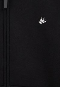 Crna majica s kapuljačom na patentni zatvarač, s malim bijelim izvezenim logom ptice na lijevoj strani prsa. Glatka tekstura tkanine s rebrastim rubom i manžetama.