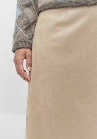 Beige faux suede kjol med slät textur, figurnära design och hög midja. En hand rör vid sidan, vilket visar på den mjuka ytan.